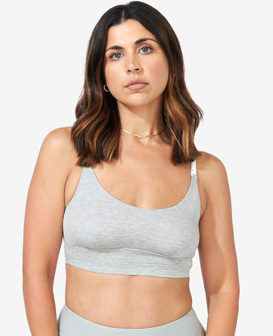 A woman with medium-length brown hair in a light gray sleeveless crop top and thin necklace stands against a plain background, looking at the camera—perfect for featuring The All-Needs Bundle • 25% off.