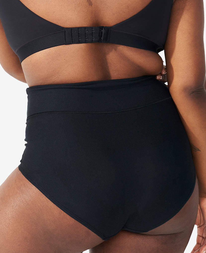 A person is shown from the back wearing The All-Needs Bundle—supportive black nursing bra and high-waisted underwear—highlighting the fit and coverage of these essentials against a plain background. Save 25% on your postpartum starter kit.