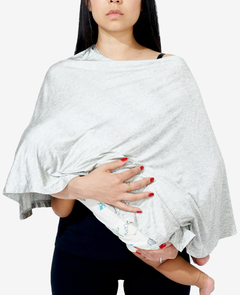 A woman with long dark hair uses a light gray nursing cover while breastfeeding a baby. Only the babys legs and feet are visible under the cover. The woman is wearing a black top and has red-painted nails. seen in Grey Marl