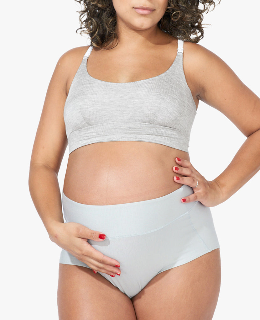 A pregnant woman in a light gray All-In Panty from the 3-Pack set (Save 16%) holds her belly and rests her hand on her hip, standing against a plain white background.