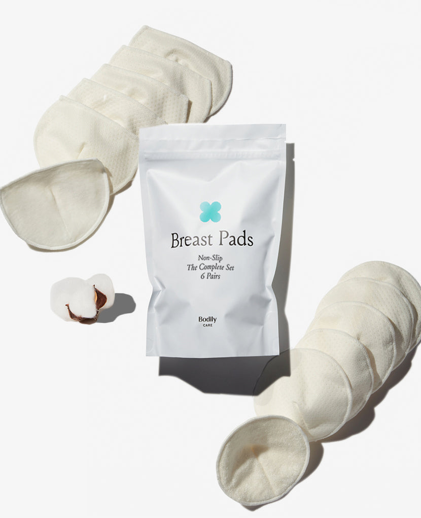 A white package labeled Breast Pads Non-Slip The Complete Set 6 Pairs is centered, surrounded by several pairs of white breast pads and a cotton boll, all laid out on a white background.
