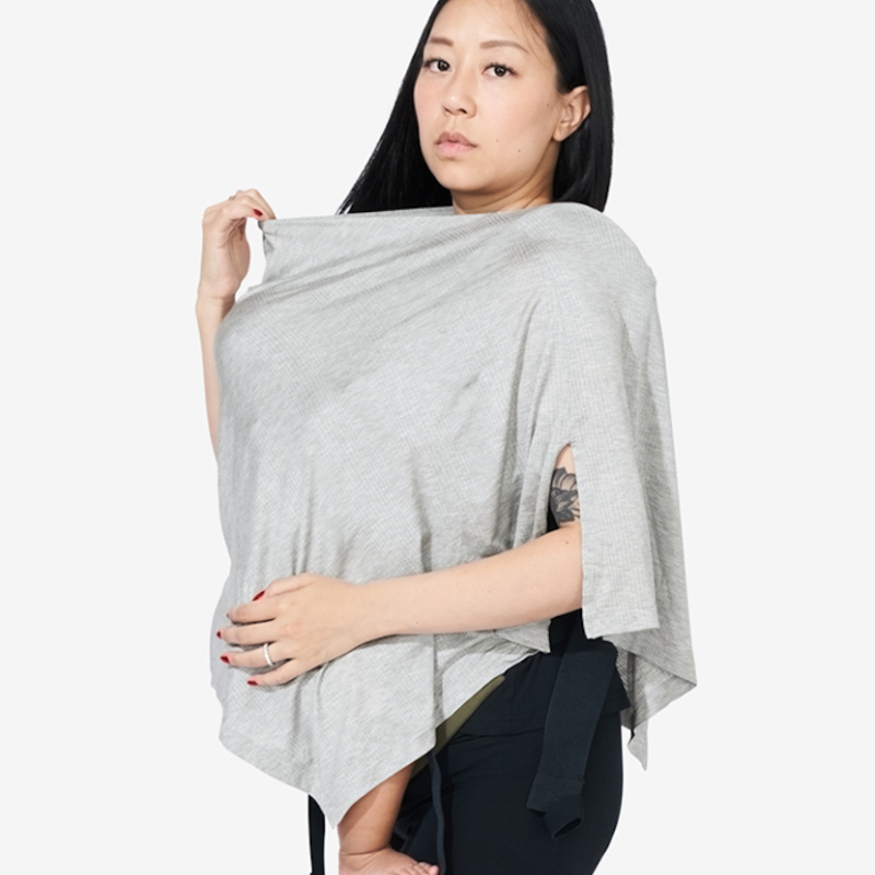 A person with long black hair wears a light gray, poncho-style nursing cover while holding a baby close to their chest. The background is plain white seen in Grey Marl