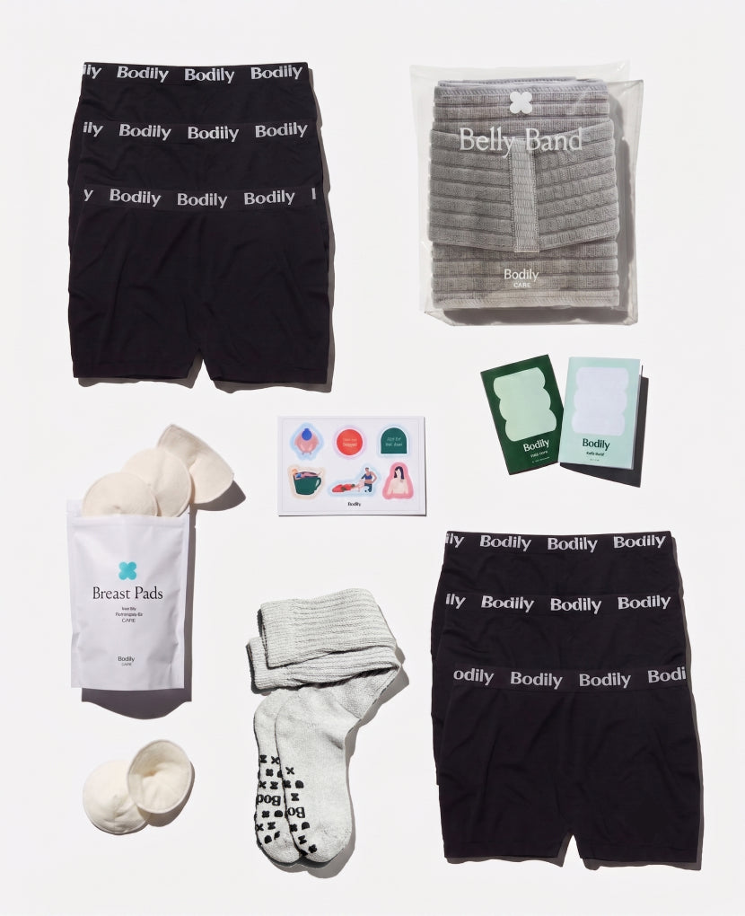 Collection of Bodily products including black boxer briefs, a belly band, breast pads, and socks on a white background.