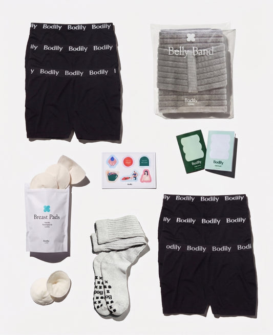 Collection of Bodily products including black boxer briefs, a belly band, breast pads, and socks on a white background.