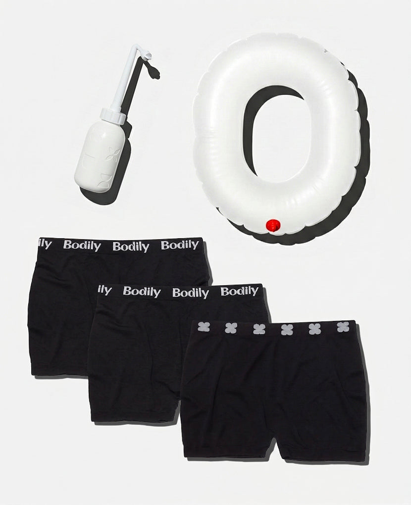 The Postpartum Recovery Kit including three black Bodily-branded underwear, a white perineal bottle, and an inflatable donut cushion—is arranged on a light background as must-have hospital bag essentials for comfort.