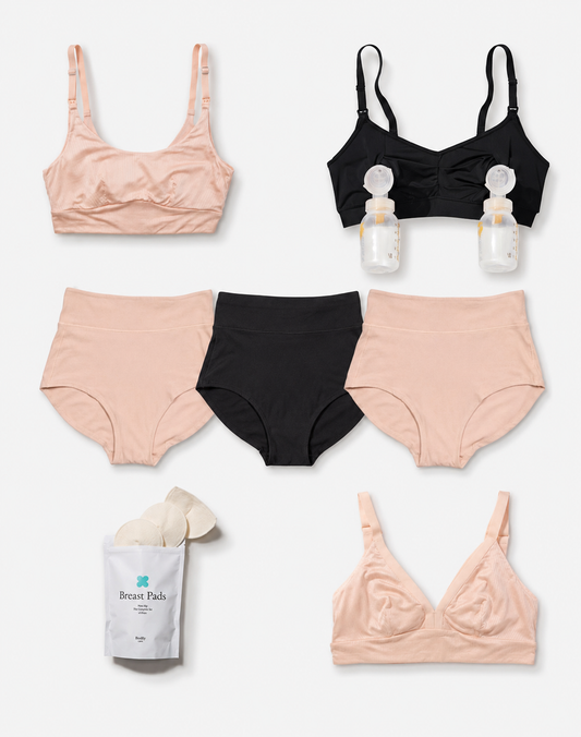 A flat lay of maternity and nursing underwear in three colors: light peach, black, and white. The set includes two light peach bras, two black high-waisted briefs, a white package of breast pads, and two clear nursing bottles with white caps.